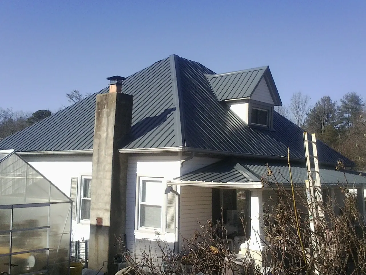 Dark blue standing seam metal roof on a white farmhouse with dormer — Slate & Tile Roof Repair by Roofing Brothers in Bonner Springs