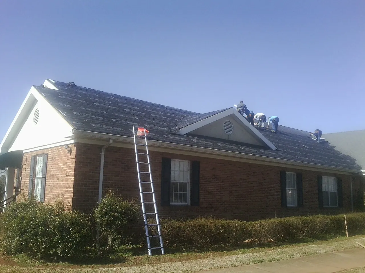 Crew tearing shingles off a brick ranch roof with a ladder set — Metal Roof Repair work by our crew in Bonner Springs