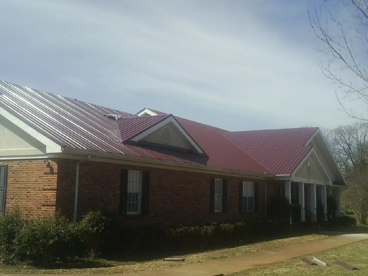 Red metal roof with gabled entries on a long brick building, from a Hail Damage Roof Repair job in Bonner Springs