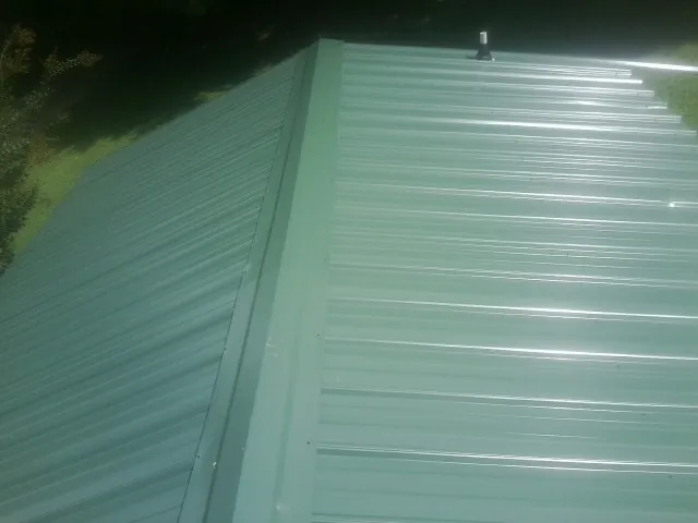 New green metal panels meeting at the ridge of a roof — Flat Roof Repair work by our crew in Bonner Springs