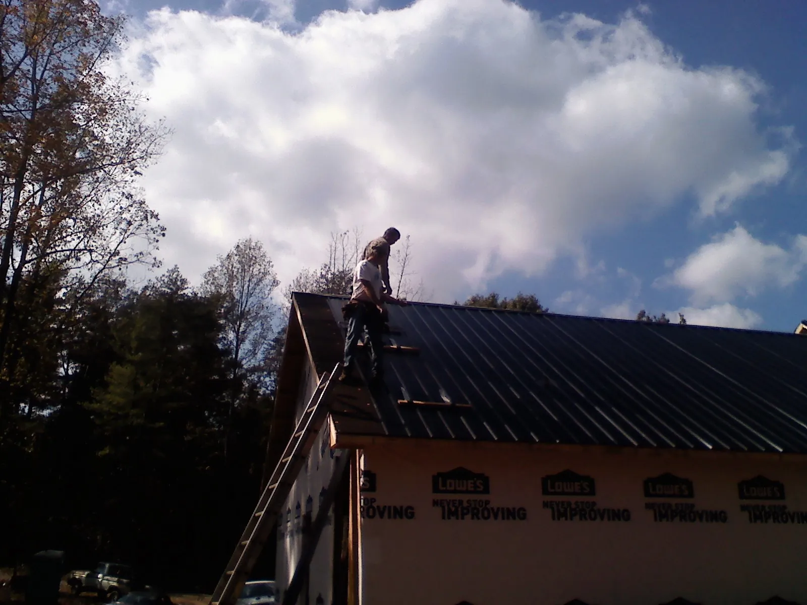 Roofer fastening dark metal panels high against a cloudy sky, from a Roof Inspection job in Bonner Springs