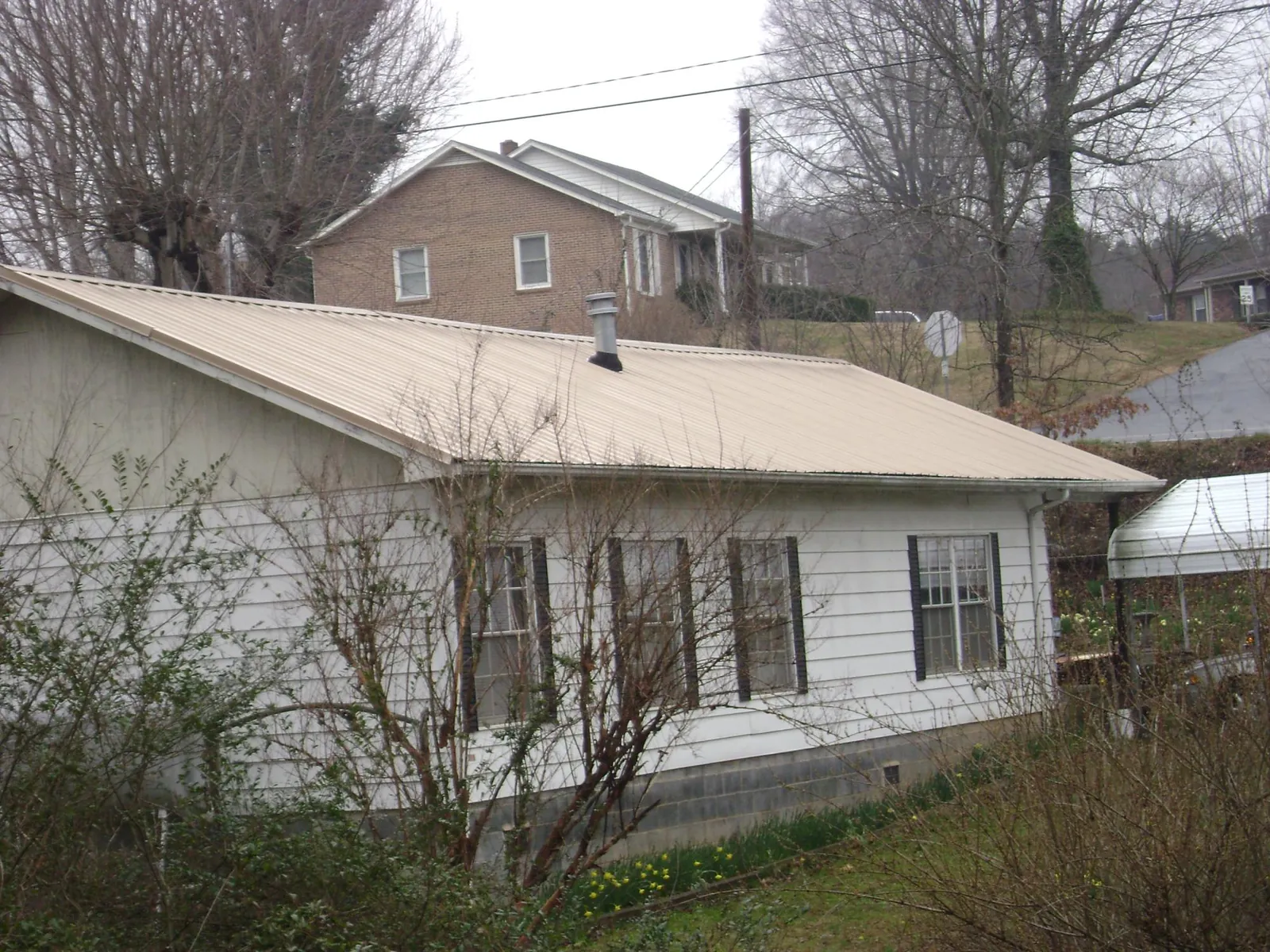 Tan metal roof on a white sided house set into a hillside — Commercial Roofing by Roofing Brothers in Bonner Springs